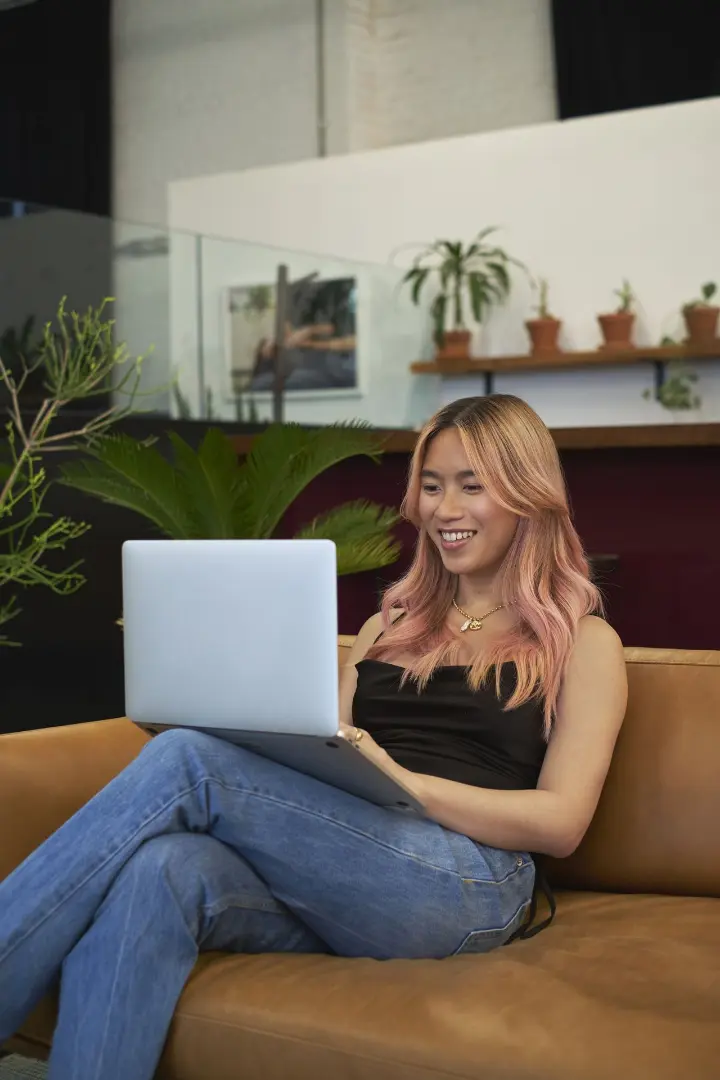 A transfeminine person smiling and using a laptop.