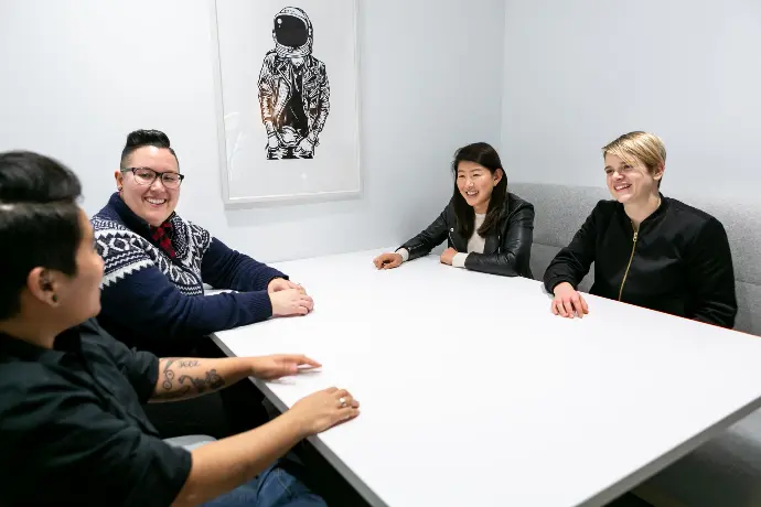 A diverse group of four folks sitting around a white table, looking happy and proud.