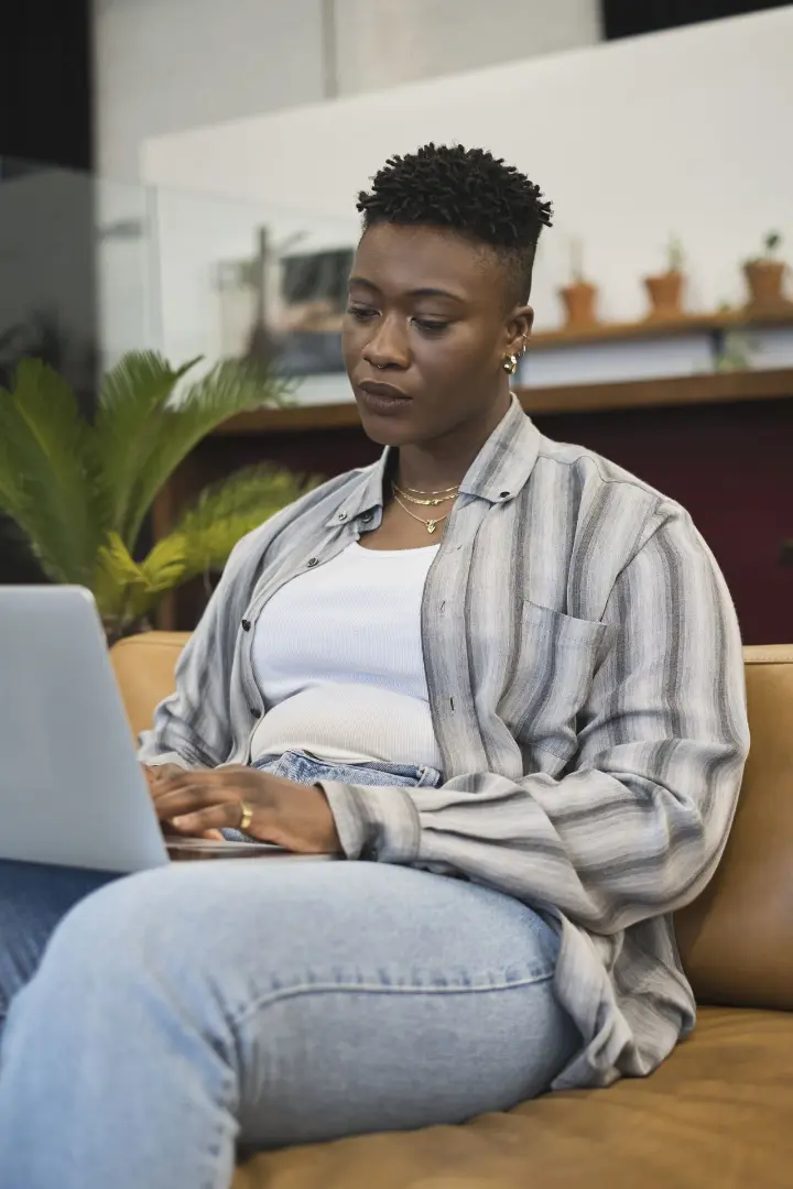A nonbinary person using a laptop at work, looking worried and frustrated.