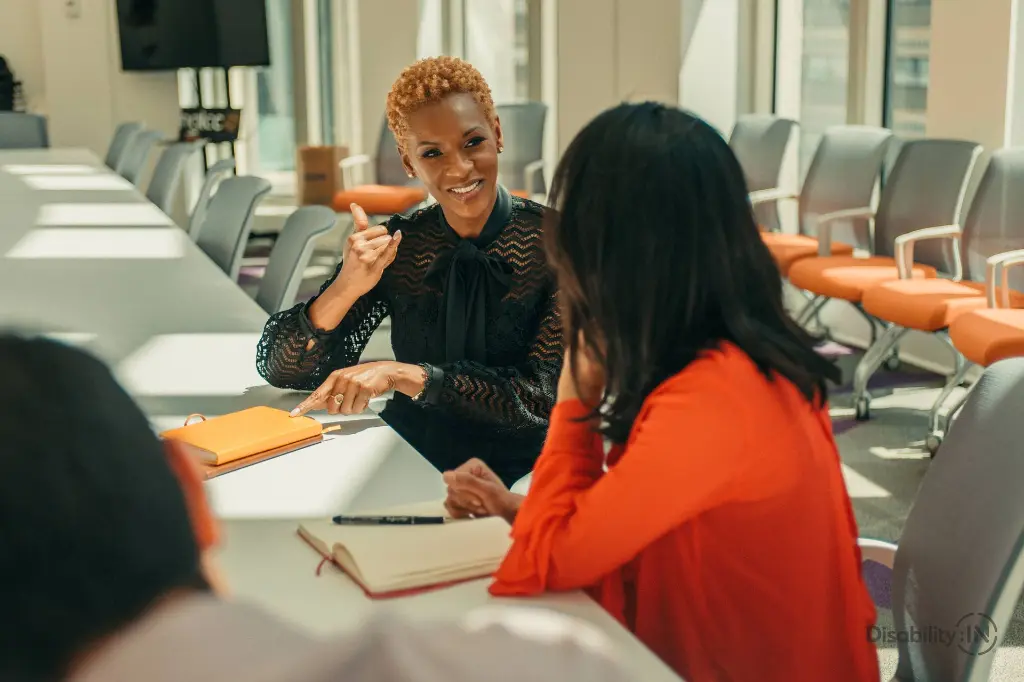 Three people of diverse ethnicities in a meeting. Two persons are actively and happily talking to each other through sign language.